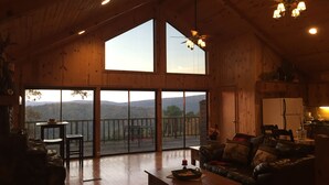 A spacious living room with a large wooden ceiling, a fireplace, a dining area, and a view of the mountains through large windows. - Beautiful and roomy two bed, two bath cabin nestled in the Kiamichi Mountains (Hodgen)