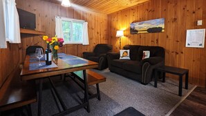 A cozy cabin interior with a wooden dining table, a sofa, and a lamp. - Amenities & Resort Access Included, Cabin 1 (Phelps)