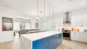 Una cocina moderna con armarios blancos, una isla azul e iluminación colgante.