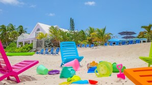 Una playa con sillas de playa coloridas, un edificio blanco con zona cubierta y un autobús al fondo.