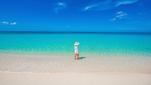Una persona de pie en una playa con agua turquesa cristalina y cielo despejado.