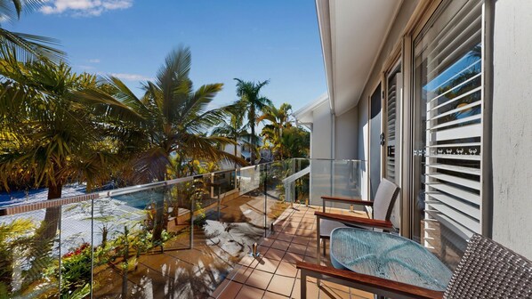 A balcony with a glass railing, outdoor furniture, and palm trees.