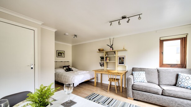 A modern, well-lit room with a bed, a desk, a sofa, and a dining area with a table set for two. - Dean Village Studio Apartment (Edinburgh)
