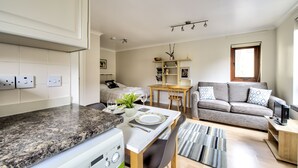 A modern kitchen with granite countertops, a dining area with a table and chairs, a sofa, and a TV on a wooden stand. - Dean Village Studio Apartment (Edinburgh)