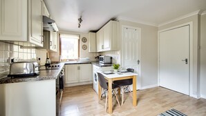 A modern kitchen with white cabinets, a dining table with chairs, a washing machine, and a microwave. - Dean Village Studio Apartment (Edinburgh)