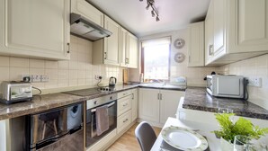 A kitchen with white cabinets, a granite countertop, a built-in oven, a toaster, and a window providing natural light. - Dean Village Studio Apartment (Edinburgh)