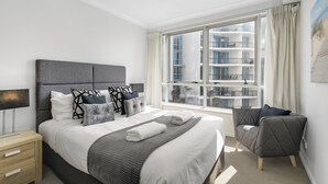Ein modernes Hotelzimmer mit einem großen Bett, einem Nachttisch, einem Sessel und einem Fenster mit Blick auf die Außenfassade des Gebäudes.