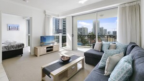Ein modernes Wohnzimmer mit Sofa, Couchtisch, Fernseher und Balkon mit Blick auf die Stadt.
