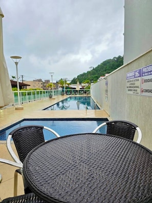 A rooftop pool area with a table and chairs, surrounded by a low fence and a sign indicating amenities.