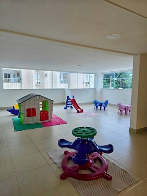 A spacious indoor play area with a small house, a slide, and various play equipment.