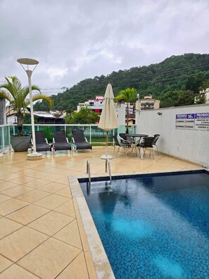 A rooftop pool area with lounge chairs, a table, and a sign indicating a prohibition on pets.