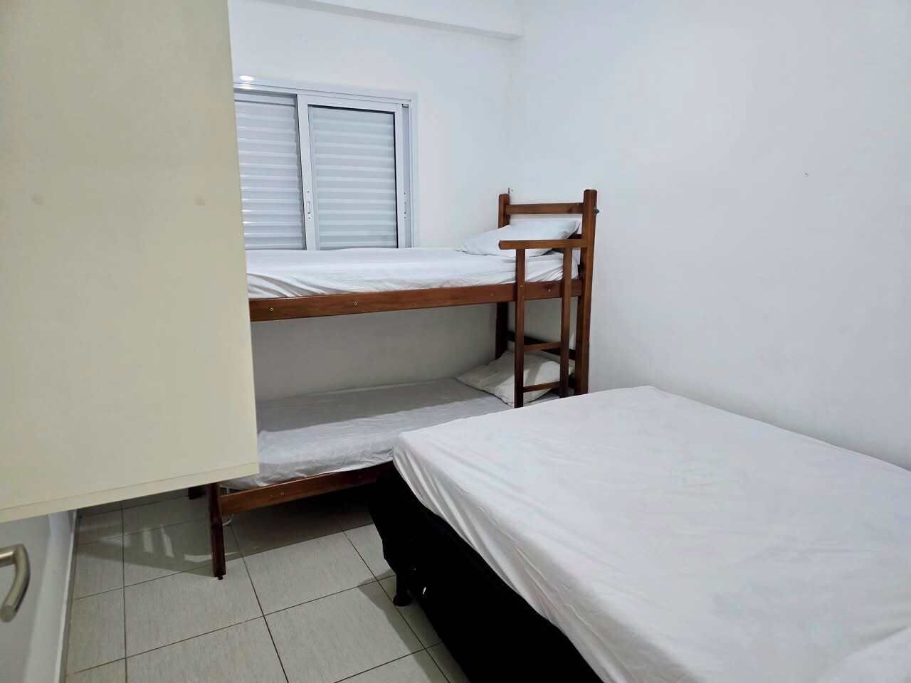 Una habitación pequeña y sencilla con una cama litera, una ventana con persianas y una puerta blanca.