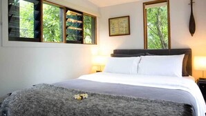 A bedroom with a bed, two windows, a framed picture, and a nightstand with a lamp.