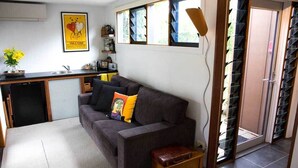 A compact living space with a sofa, a small table, a kitchen area with a sink, and a sliding glass door leading to a balcony.