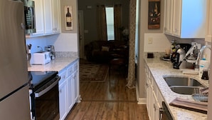 A kitchen with white cabinets, a stainless steel refrigerator, a built-in oven, a microwave, a sink, and a coffee maker.