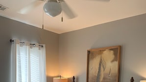 A bedroom with a four-poster bed, a painting of a sailboat, and a ceiling fan.