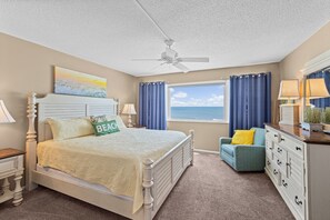 A bedroom with a bed, a dresser, a nightstand, a window with curtains, and a ceiling fan.
