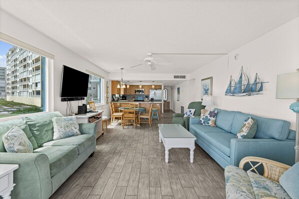 A modern living room with a sofa, coffee table, and a TV. There is a kitchen area with a dining table and chairs.