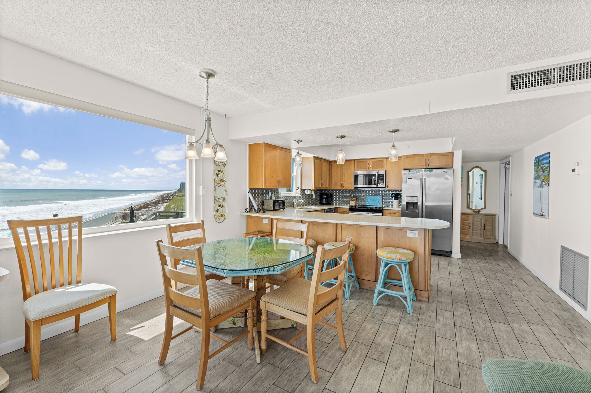 A modern kitchen with wooden cabinets, a glass dining table, and a view of the ocean.