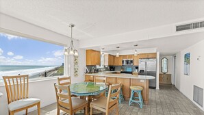 A modern kitchen with wooden cabinets, a glass dining table, and a view of the ocean. - Oceanfront 2BR Condo w/ Balcony & Panoramic Atlantic Views, Unit 226 (Satellite Beach)