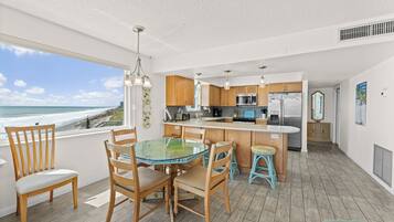 A modern kitchen with wooden cabinets, a glass dining table, and a view of the ocean.