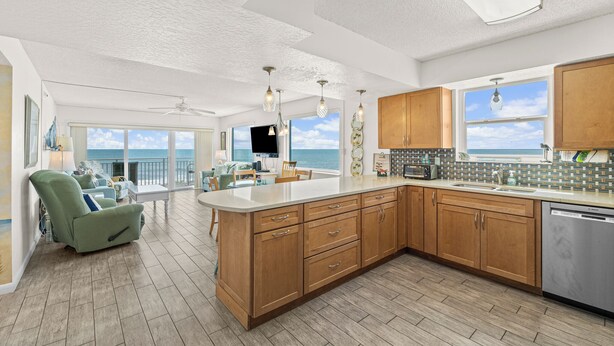 A spacious kitchen with wooden cabinets, a large island, and a view of the ocean. - Oceanfront 2BR Condo w/ Balcony & Panoramic Atlantic Views, Unit 226 (Satellite Beach)