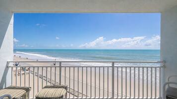 A balcony with a view of the beach, a railing, and a few lounge chairs.