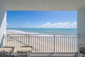 Un balcón con vista a la playa, una barandilla y algunas sillas de descanso.