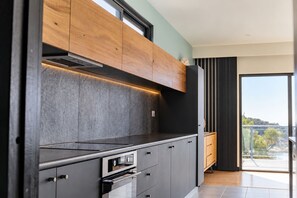 Una cocina moderna con armarios oscuros, una campana extractora de acero inoxidable y un amplio ventanal con vistas al exterior.