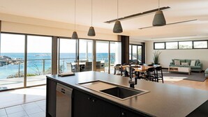 Una cocina moderna con una isla grande, comedor y amplios ventanales con vistas al mar.