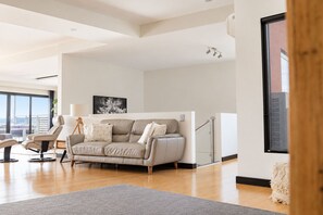 Una sala de estar moderna con un sofá gris, una mesa de centro de madera y una alfombra gris. Se ve una escalera que sube a un nivel superior.