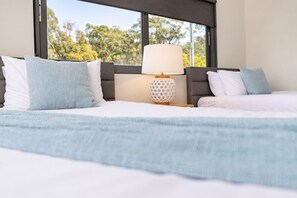 Habitación de hotel con cama, mesita de noche, lámpara y ventana con vistas a árboles.