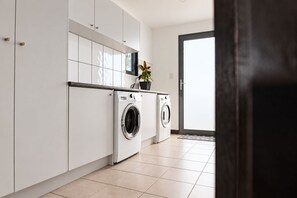 A modern kitchen with white cabinetry, a built-in washing machine, and a potted plant.