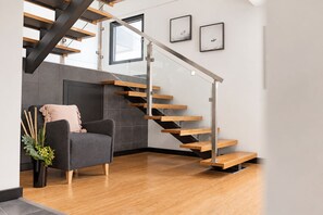 Un interior moderno con una escalera de madera, un sofá gris y una chimenea.