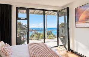 A bedroom with a bed, a view of the ocean, and a balcony with a railing.