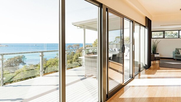 Un interior moderno con puertas de cristal amplias que dan a un balcón con vistas a un cuerpo de agua.