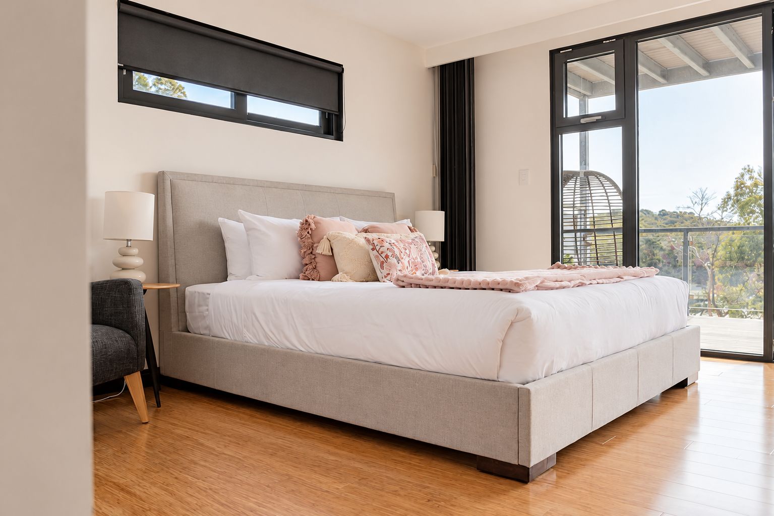 A modern bedroom with a large bed, a side table, a lamp, and a view through a large window.