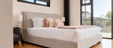 A modern bedroom with a large bed, a side table, a lamp, and a view through a large window.