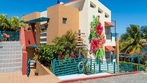 A building with a staircase, a blue fence, and a sign with multiple directions. - Room with a View! Stay LOVE PLAY on the beach in Isabela, between Jobos & Shacks (Isabela)