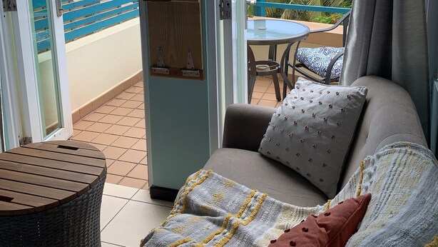 A balcony with a view of palm trees, a wooden table, and a sofa with cushions. - Room with a View! Stay LOVE PLAY on the beach in Isabela, between Jobos & Shacks (Isabela)