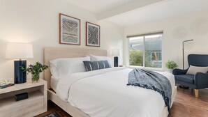 Um quarto moderno com uma cama grande, mesas de cabeceira, uma cadeira e obras de arte nas paredes.