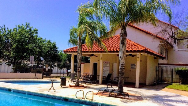 Zona de piscina amb una piscina blava cristal·lina, gandules i un edifici amb teulada vermella.