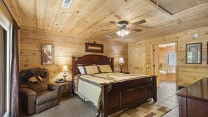 Une chambre à coucher aux murs lambrés, avec un lit, une table de chevet, une lampe, une chaise et un ventilateur de plafond.