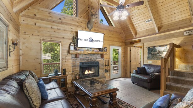 L’intérieur d’une cabane en rondins, avec une cheminée, des canapés en cuir, une tête de cerf accrochée au mur et une enseigne indiquant « RENTBRINSON.COM ».