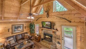 L’intérieur d’une cabane en rondins, avec une cheminée en pierre, un canapé en cuir et une tête de cerf fixée au mur.