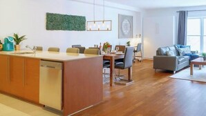 Una cocina moderna con lavavajillas, un comedor con sillas, un sofá gris y un amplio ventanal.