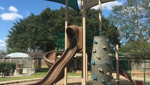 A playground structure with a slide, climbing wall, and shaded area. - Super Bowl Head Quarter,NRG,Minute Maid,Convention,MedCenter,MdAnderson,Galleria (Houston)