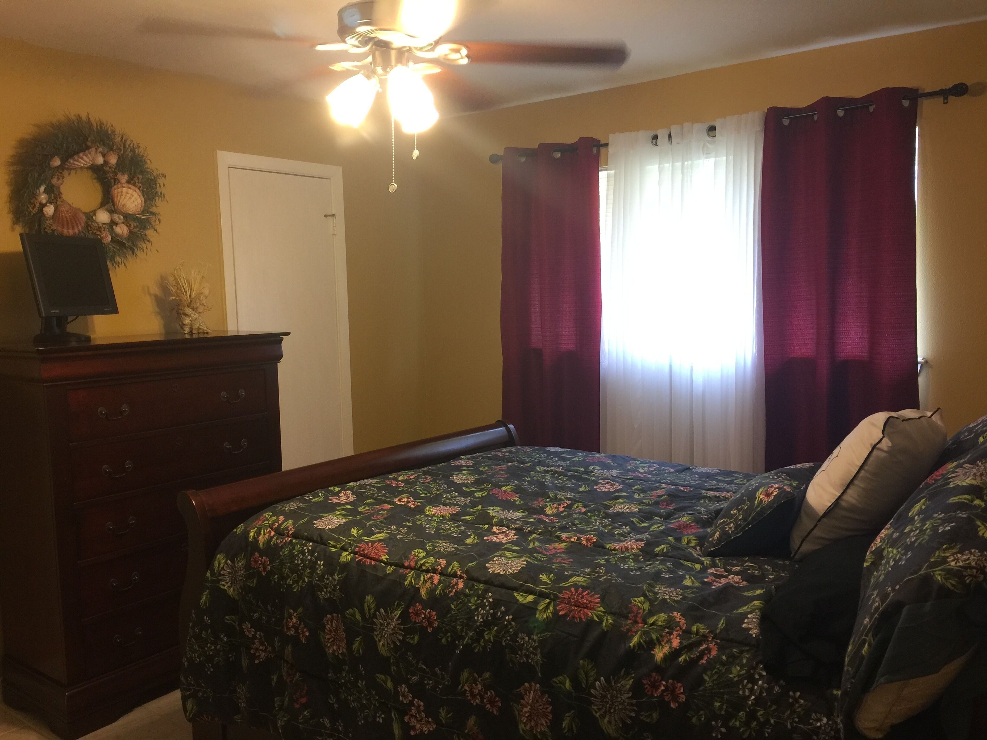 A bedroom with a bed, a dresser, a ceiling fan, and a window with curtains.