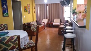 A living room with a sofa, chairs, a small table, and a TV mounted on the wall. - Apartment for rent in Caldas Novas (Do Turista)