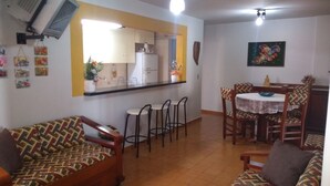 A living room with a sofa, a dining table with chairs, and a kitchen area with a refrigerator and cabinets. - Apartment for rent in Caldas Novas (Do Turista)